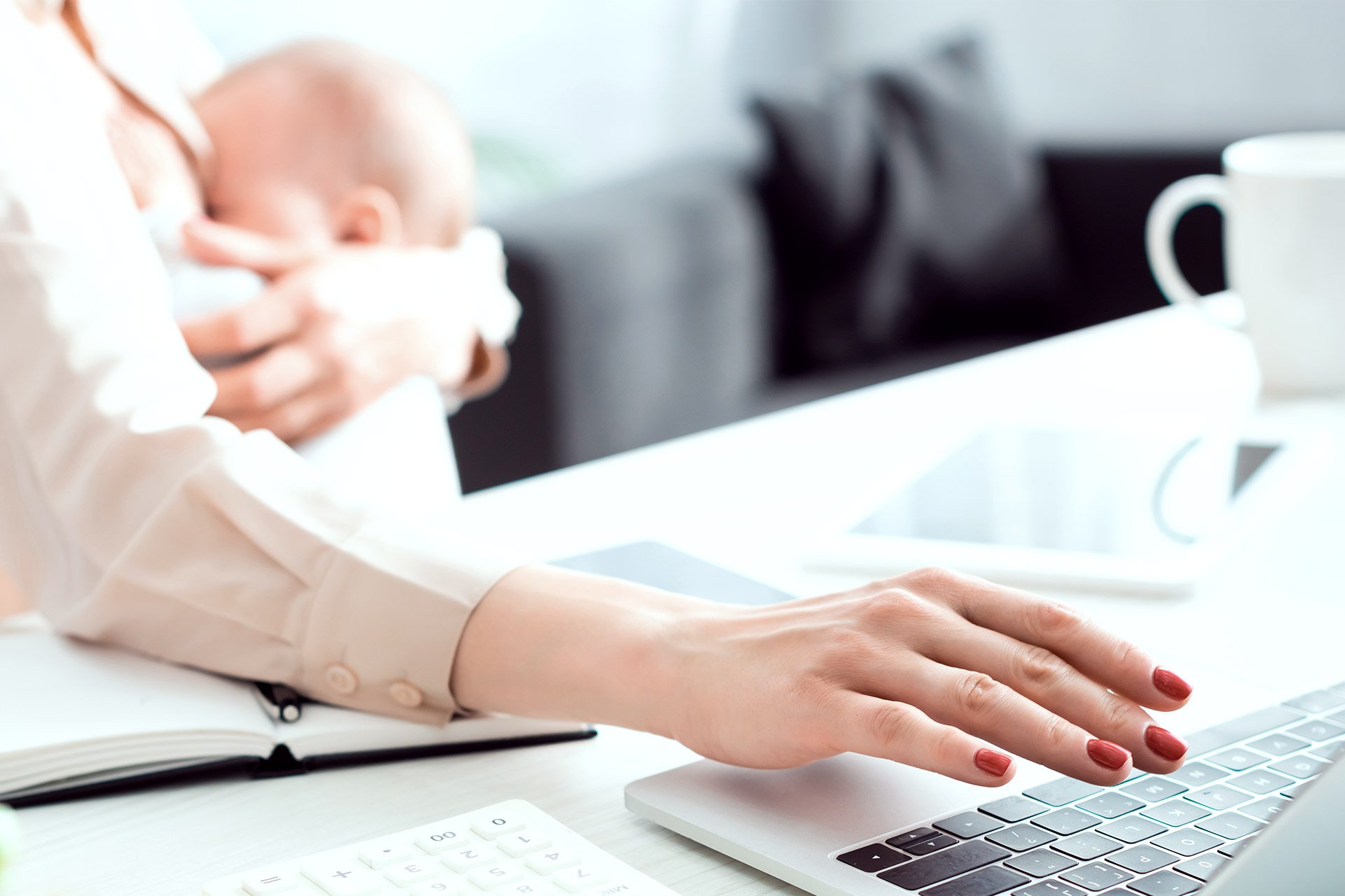 Mamá trabajando en el computador con su bebé en brazos