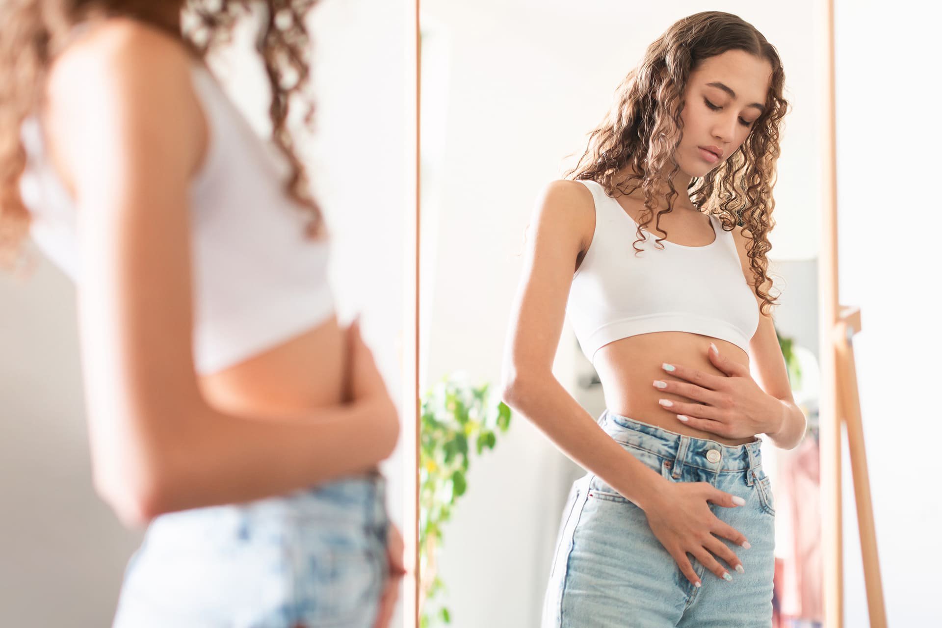 Mujer tocando su barriga frente al espejo.