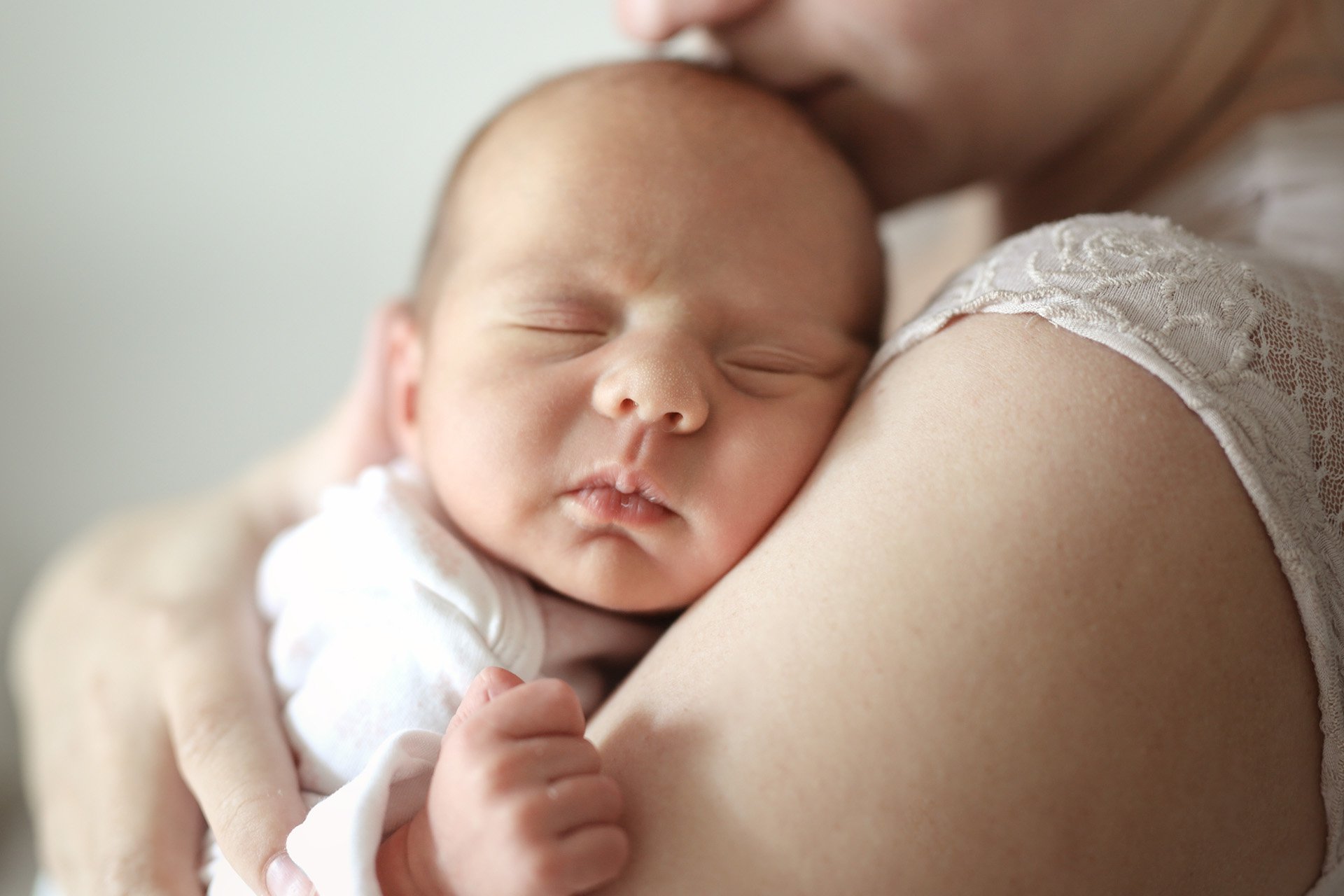 Bebé recién nacido dormido en brazos de su mamá.